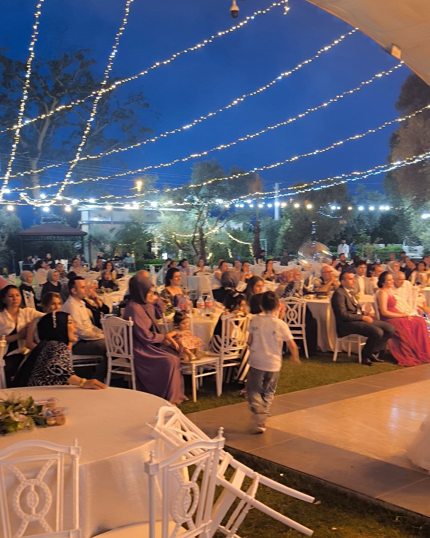 Mavi saatte ışık zincirlerinin altındaki yemek masaları